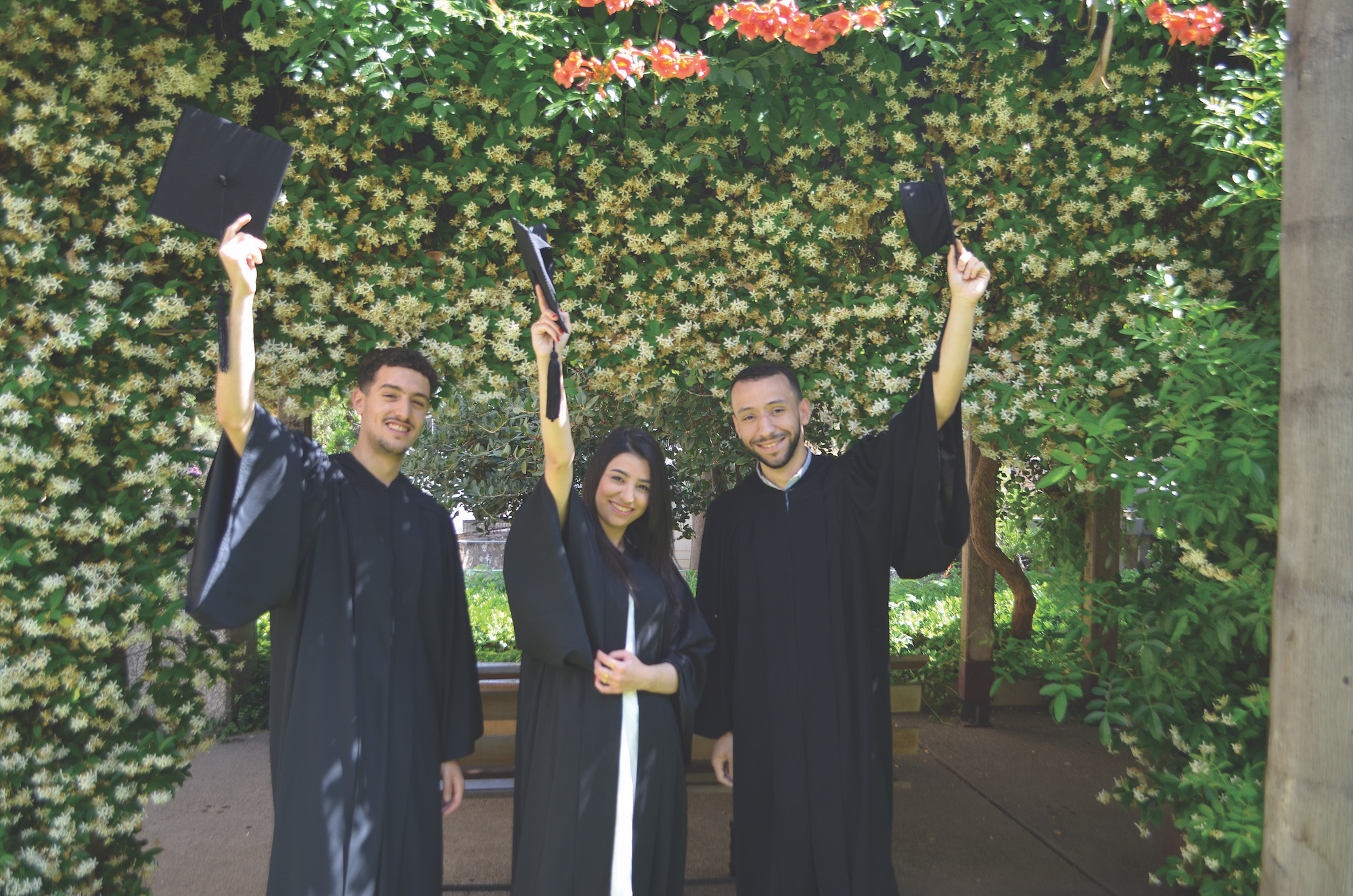 Two male graduates and one female graduate in cap and gown.